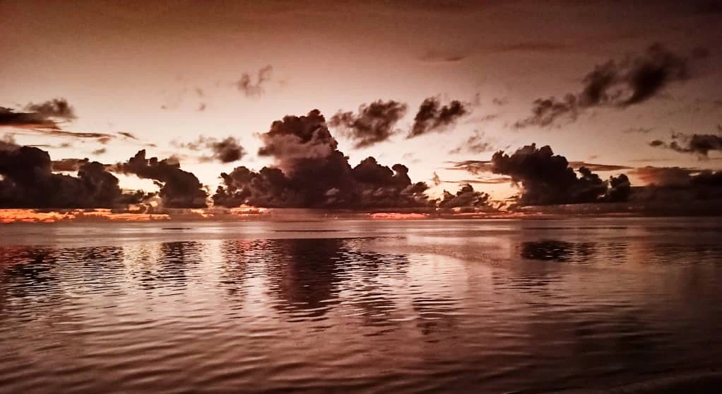 Sunrise over the lagoon at Pongwe, storm clouds on the horizon reflected in the still water