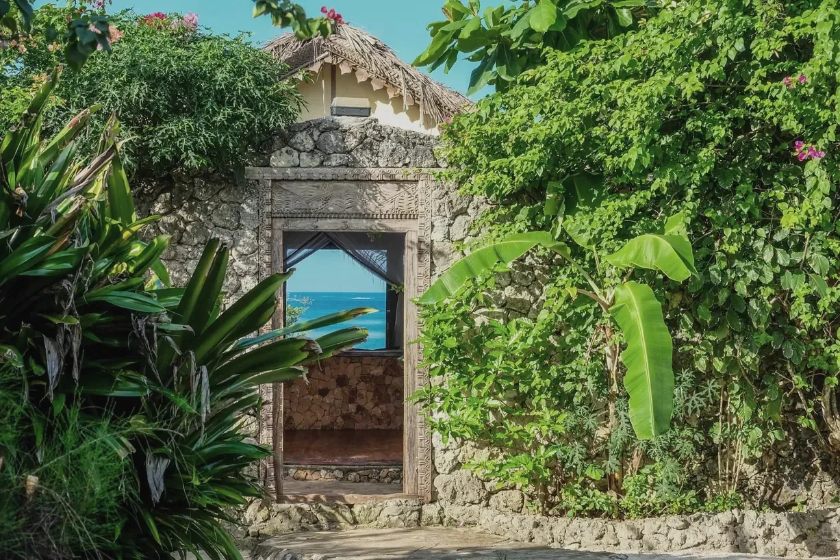 A carved Swahili door at Seasons Lodge, open on to a glimpse of the sea through the bougainvillea